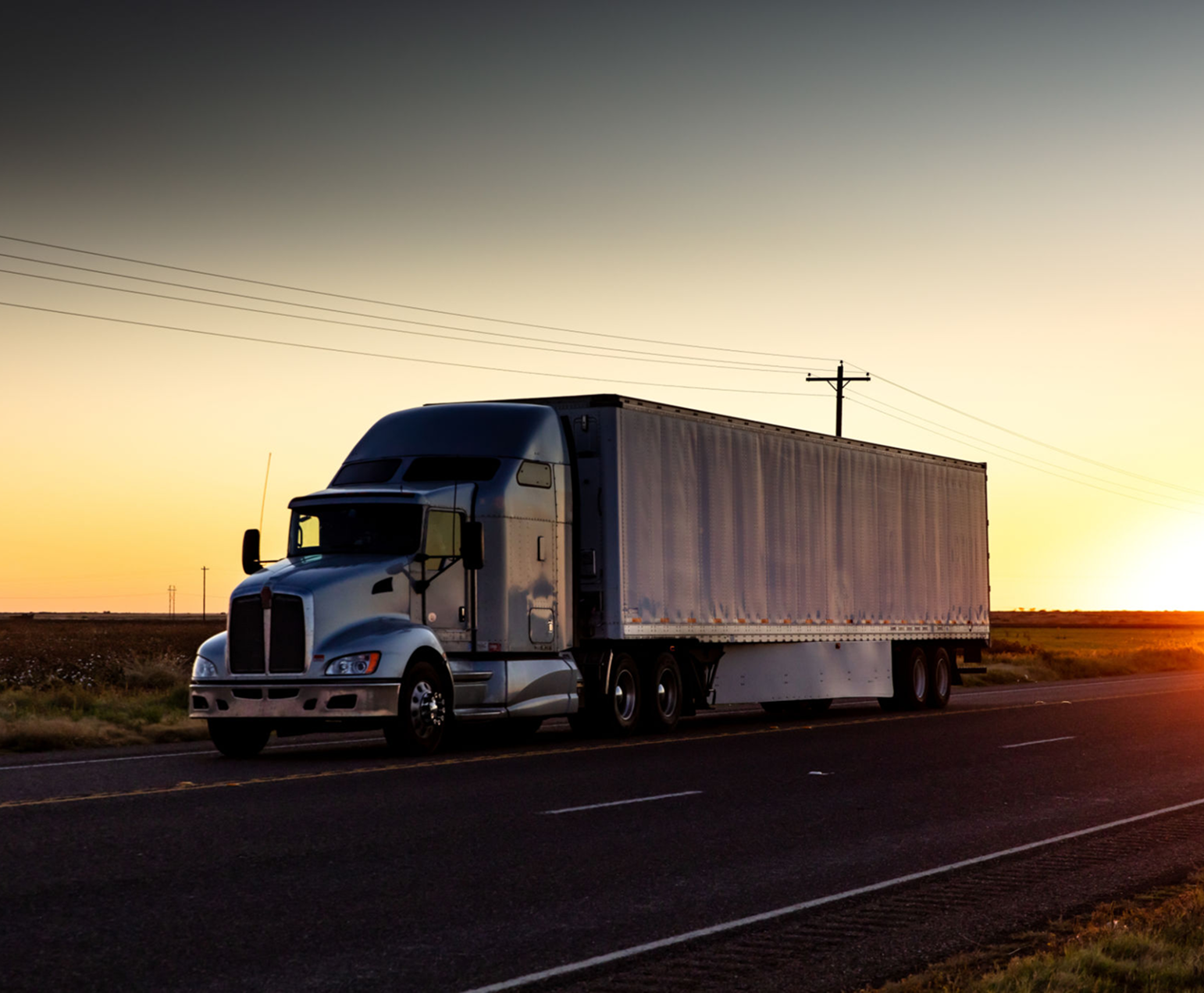Semi-truck driving on highway at sunset.