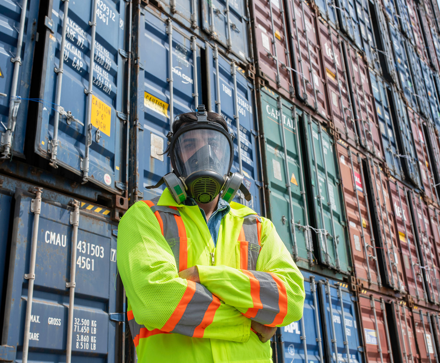 Worker in safety gear by shipping containers.