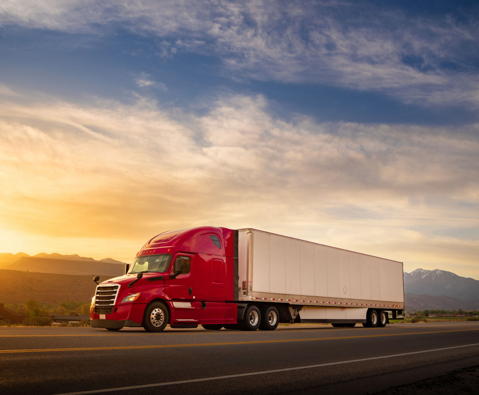 Red truck driving on highway at sunset.